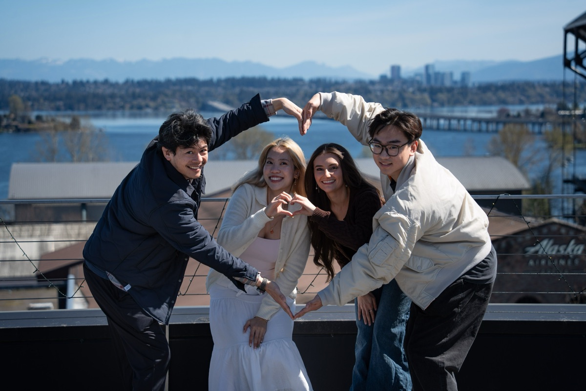 The four teammates on the same rooftop, making a heart together with their arms.