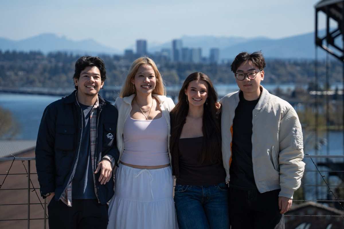 The four teammates standing together on a rooftop, a lake and city skyline behind them.